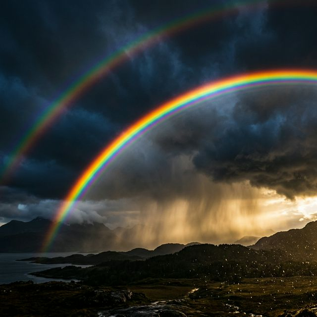 Vivid double rainbow arcing across dark stormy sky with rain droplets catching sunlight